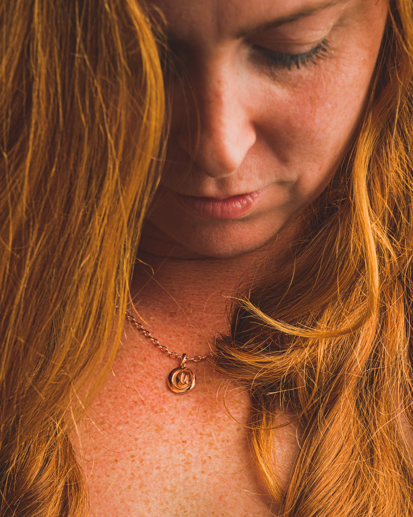 Woman wearing coppered MECFS signature rose gold pendant